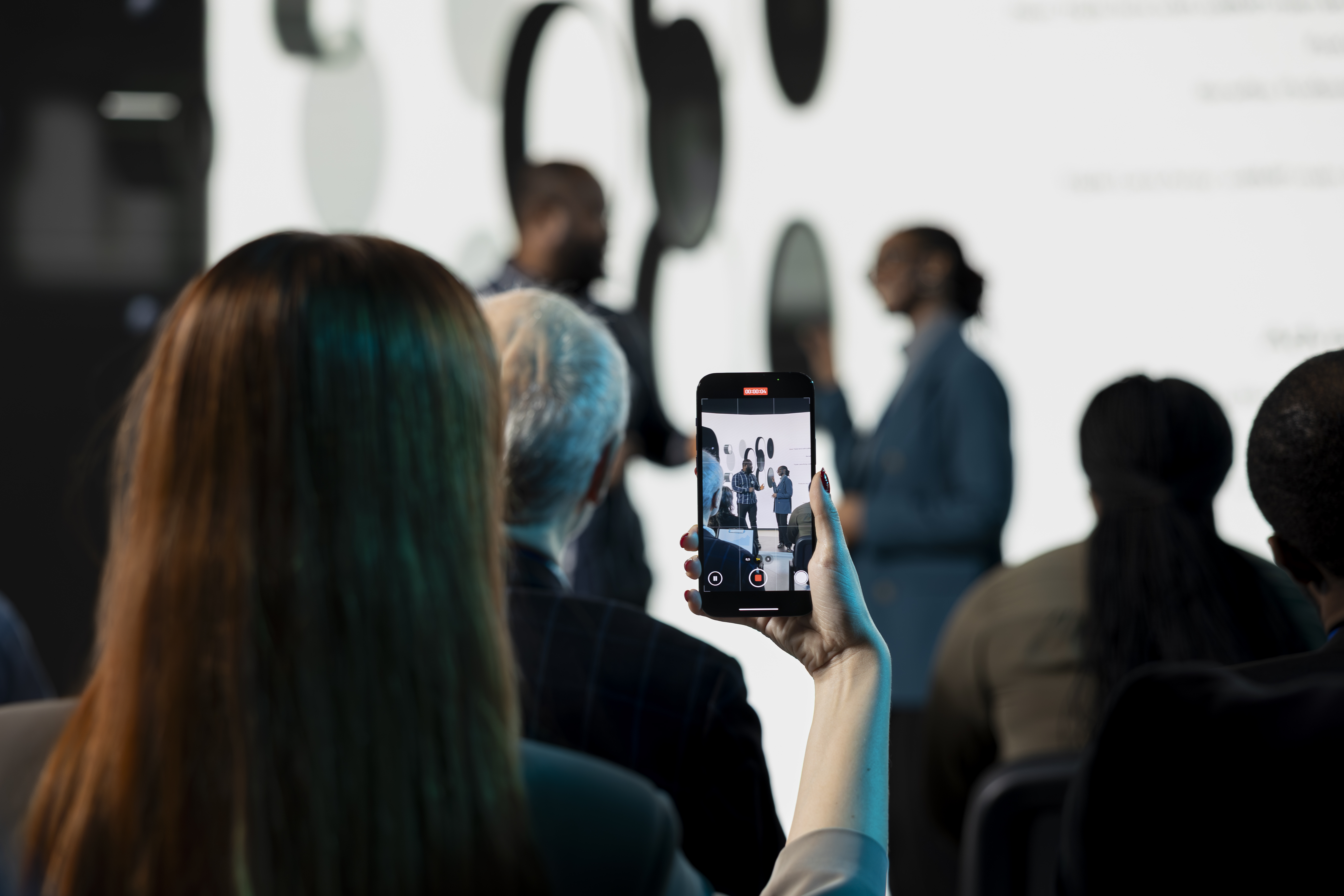 Audience watching presentation recorded on phone 2026 01 19 15 28 42 utc